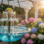 Blue hanging bird bath with two tier fountain in front of flowers.