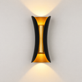 Black and gold outdoor wall sconce mounted on a light wall, casting warm light upward and downward.