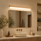 Wooden wall sconce glowing above a rounded bathroom mirror with plants and a white basin.
