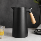 A jet black insulated carafe with a pale wood handle on a charcoal backdrop.