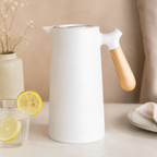 A pearl white insulated carafe with a pale wood handle beside lemon water.