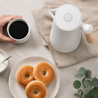 A pearl white insulated carafe sits beside coffee and pastries on neutral linen.