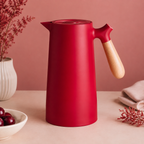 A ruby red insulated carafe with a pale wood handle on a muted rose backdrop.