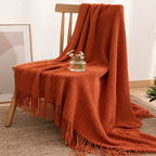 Burnt orange knit throw blanket draped over a wooden chair beside a small vase