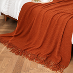 Burnt orange knit throw blanket close up showing textured stitches and fringe