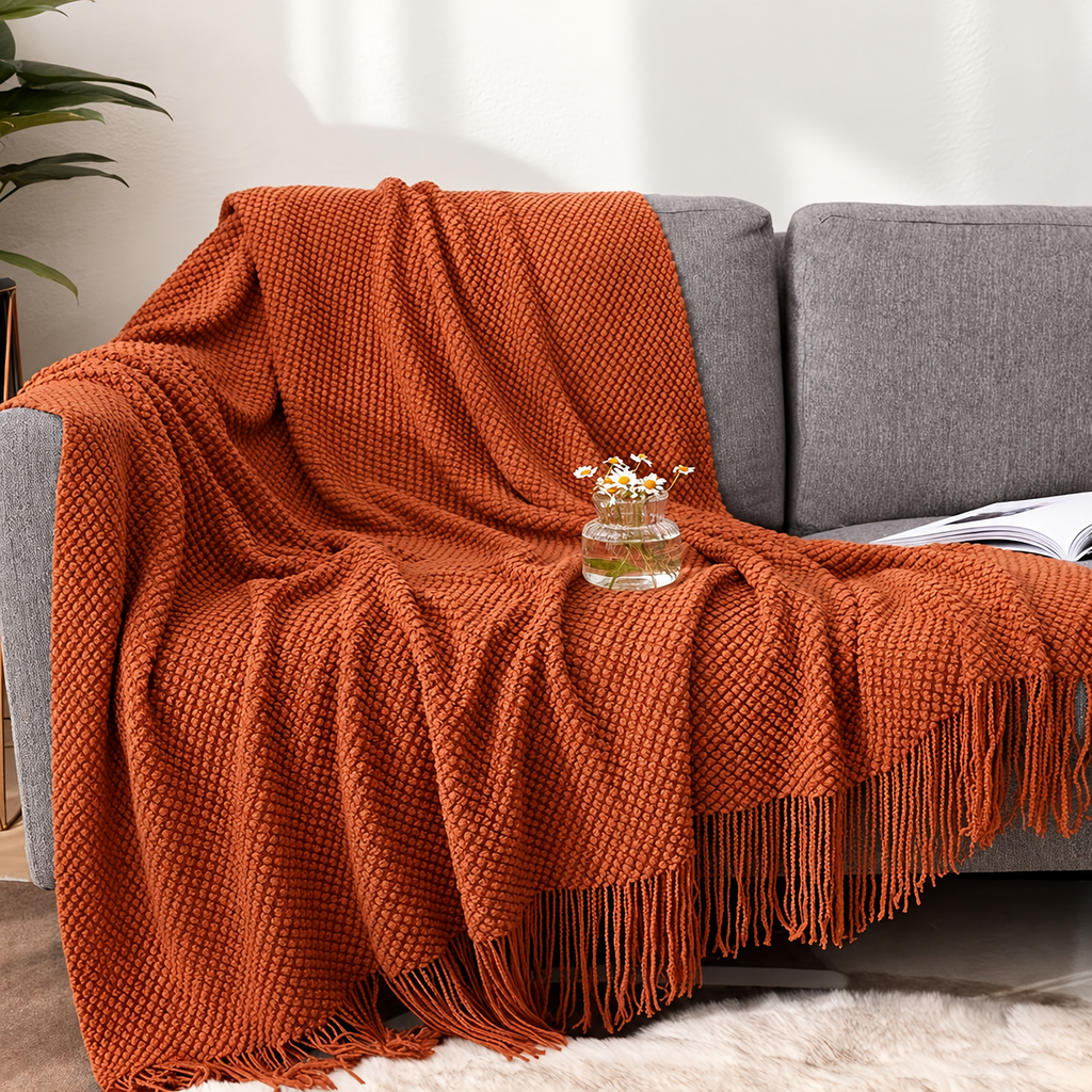 Burnt orange knit throw blanket draped across a gray sofa