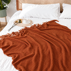 Burnt orange knit throw blanket spread across white bedding