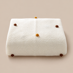 Folded white acrylic knit throw blanket showing colored pom pom dots