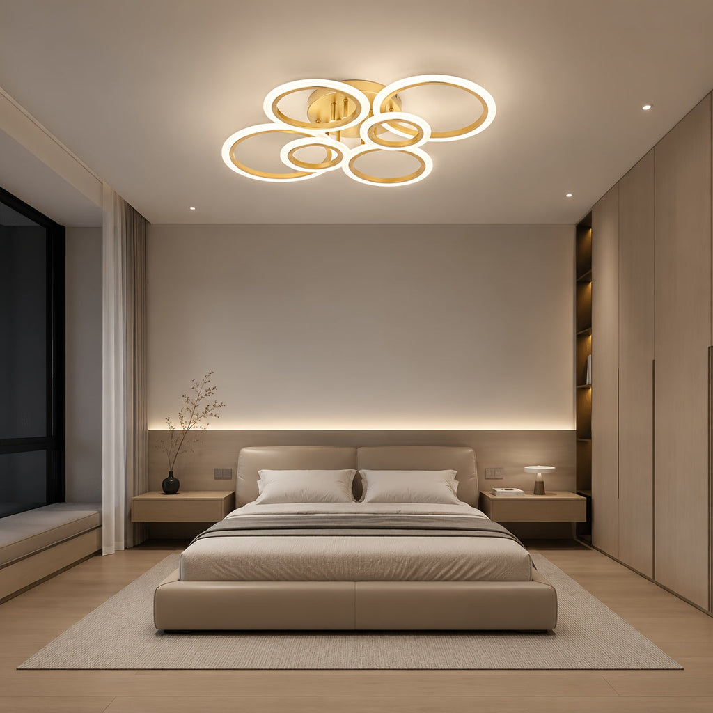Gold six ring LED ceiling light above a bed in a neutral bedroom.