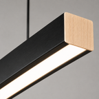 Linear pendant light close-up showing the black rectangular frame, wood-tone end cap, and glowing diffuser.