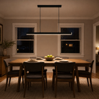 Black linear pendant light hanging above a rectangular dining table in a warmly lit room at night.