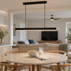 Black linear pendant light hanging over a round dining table in an open living and dining area.