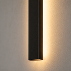 Close-up wall sconce casting warm light upward and downward on a dark wall.
