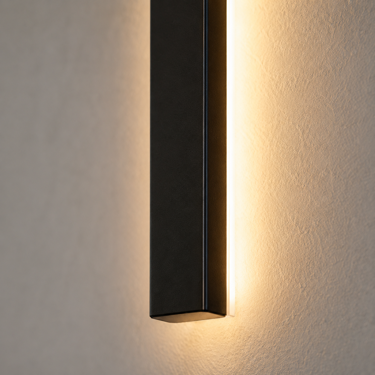 Close-up wall sconce casting warm light upward and downward on a dark wall.
