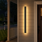 Vertical wall sconce casting warm light on a wooden exterior wall at dusk.