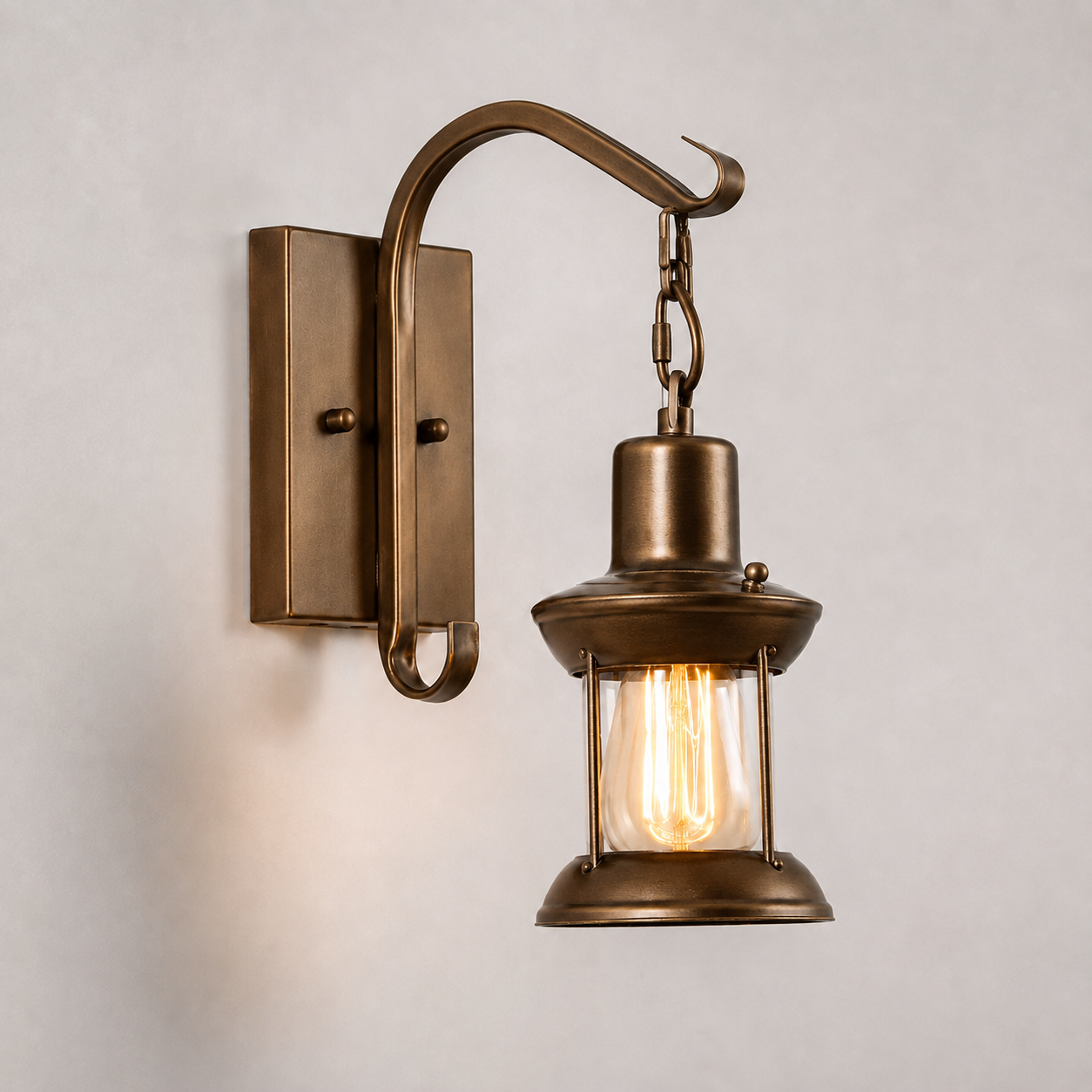 Brass lantern wall sconce with a curved arm and exposed warm glowing bulb on a neutral wall.