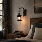Black lantern wall sconce casting warm light beside a bed in a dark bedroom.