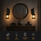 Two black lantern wall sconces casting warm light beside a round mirror and console table.