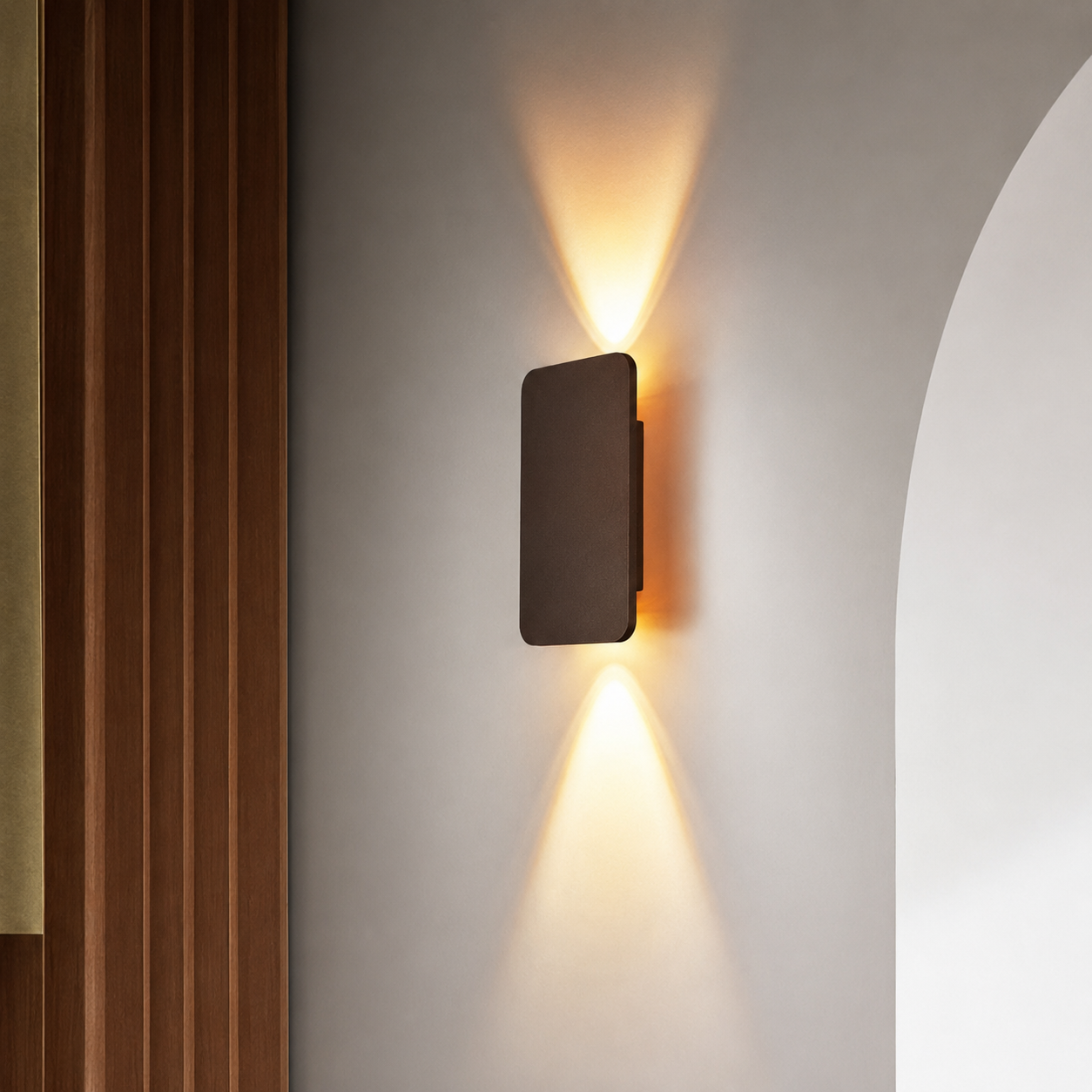 Bronze rectangular wall sconce casting warm upward and downward light beside wood panels.