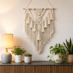 Natural macrame wall hanging centered above a console with potted plants.
