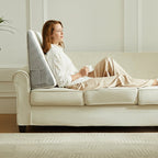 Woman seated against an upright gray wedge pillow on a sofa.