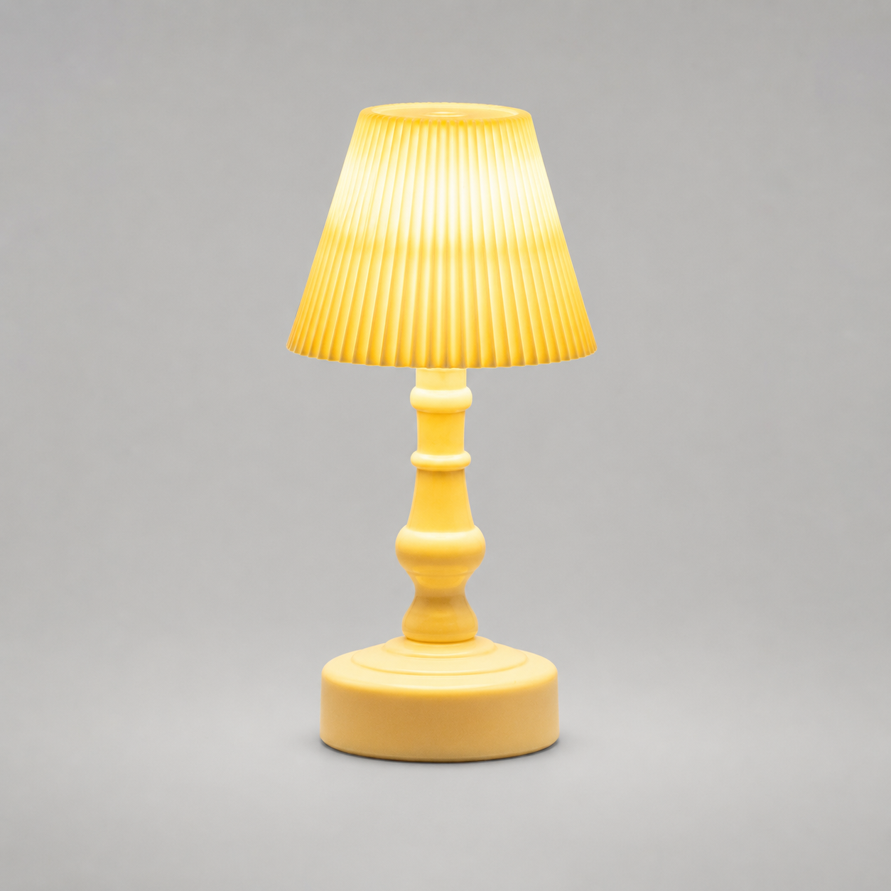 A small yellow table lamp with a pleated fabric shade, a turned wooden-style stem, and a round base, shown against a plain gray studio background.