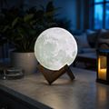 White 3D printed moon lamp glowing on a wooden bedside table
