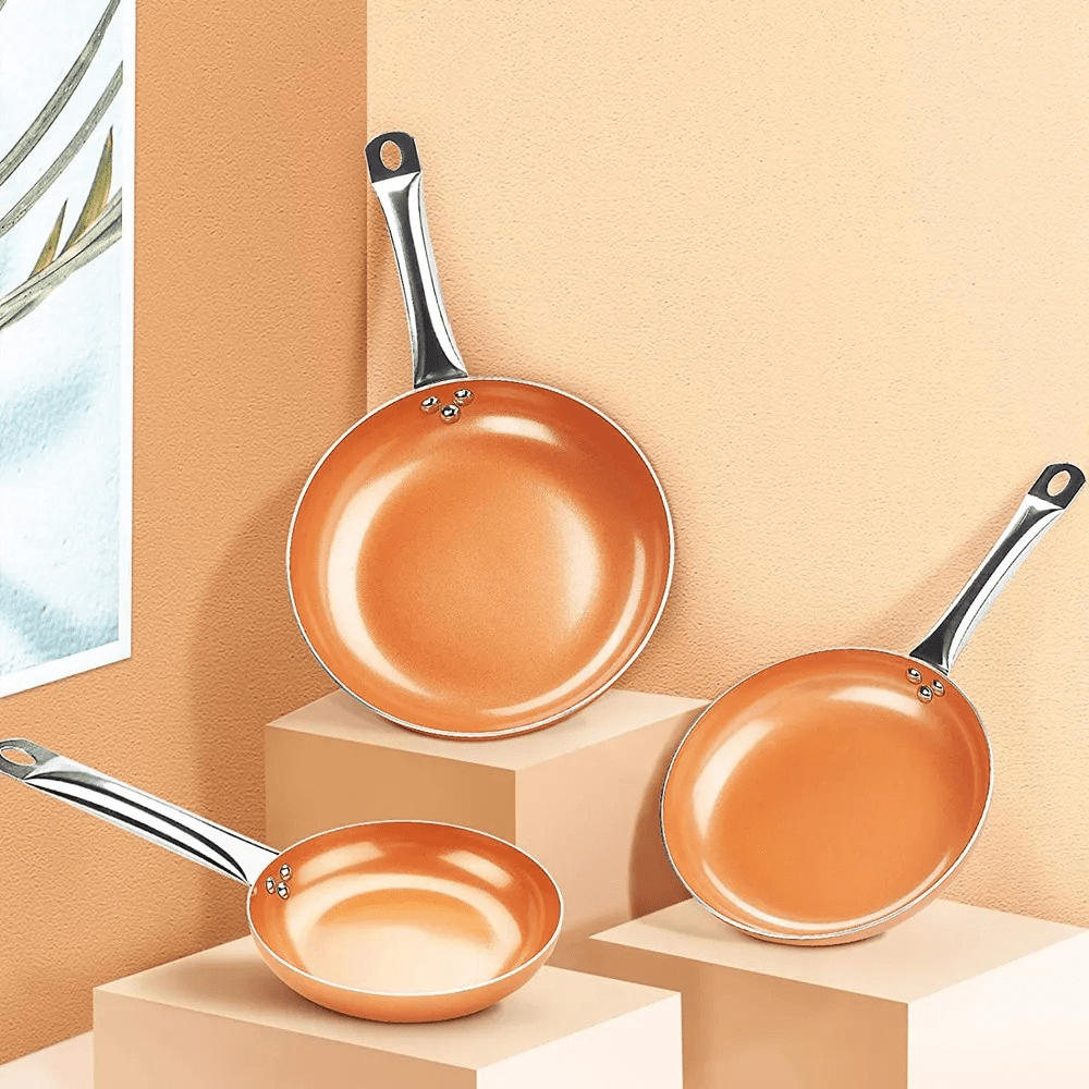 Three copper frying pans in graduated sizes arranged on display blocks.