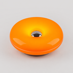 A glossy orange donut-shaped light or lamp with a metallic silver center and a dark base, shown on a light gray background.