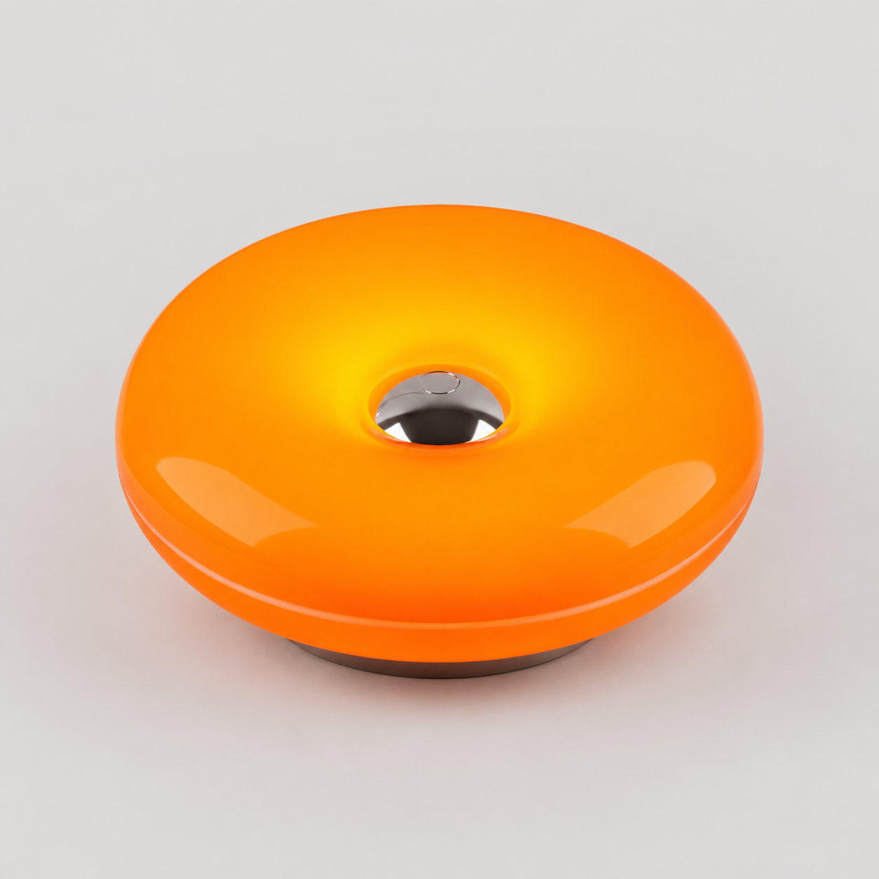 A glossy orange donut-shaped light or lamp with a metallic silver center and a dark base, shown on a light gray background.