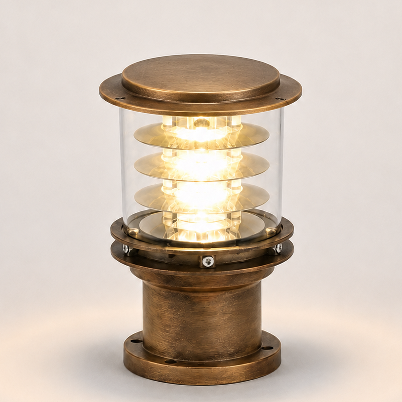 A vintage-style industrial table lamp with a brass-colored metal base and top cap, a clear glass cylinder, and a glowing spiral filament bulb inside, set against a plain light gray background.