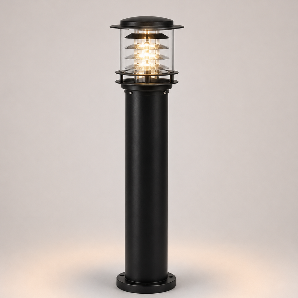 A modern black outdoor bollard light with a clear glass shade and warm glowing LED light, set against a neutral light gray background.