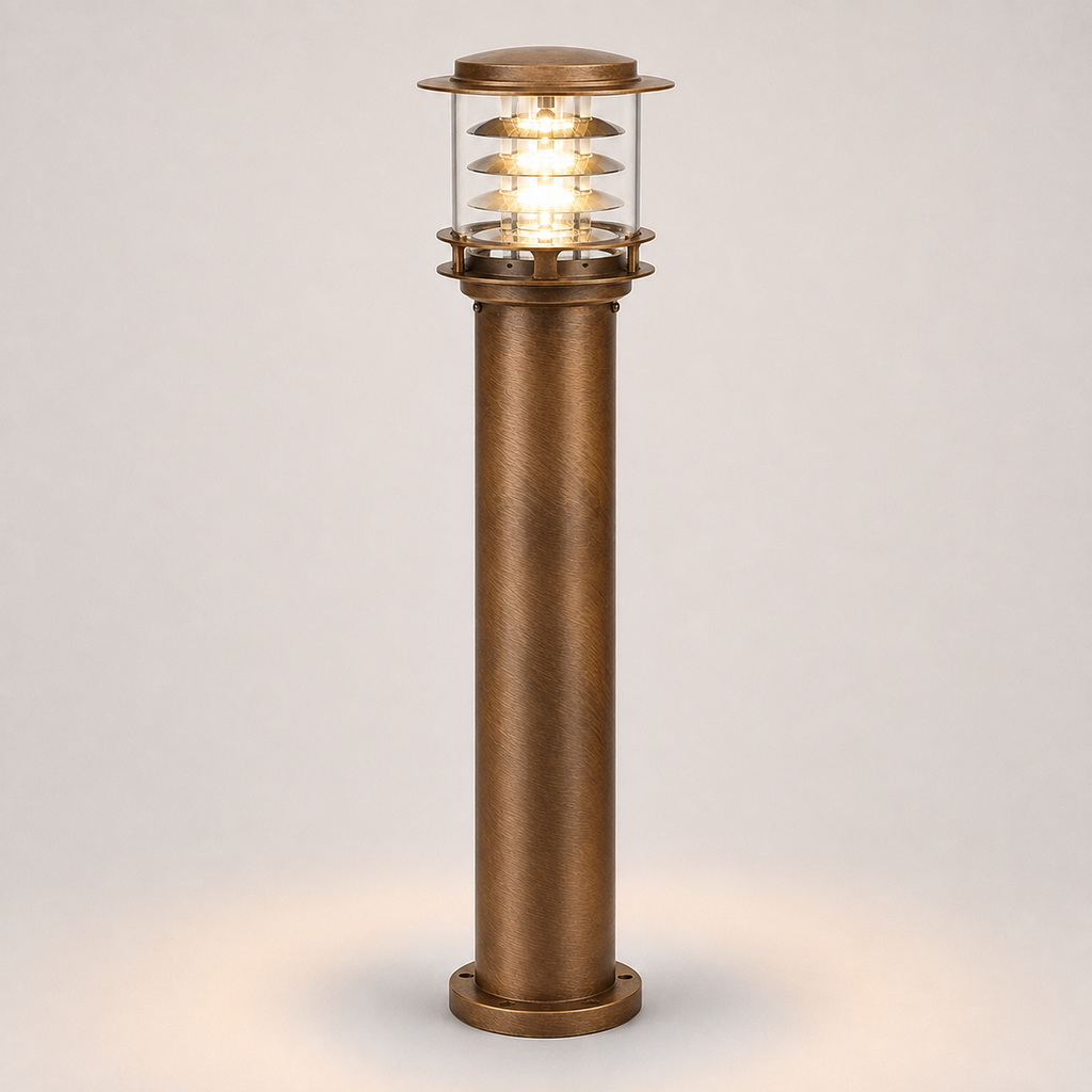 A single outdoor bollard post light with a textured bronze column and a clear glass top section showing a warm glowing light, set against a neutral light gray background.