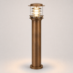 A single outdoor bollard post light with a textured bronze column and a clear glass top section showing a warm glowing light, set against a neutral light gray background.