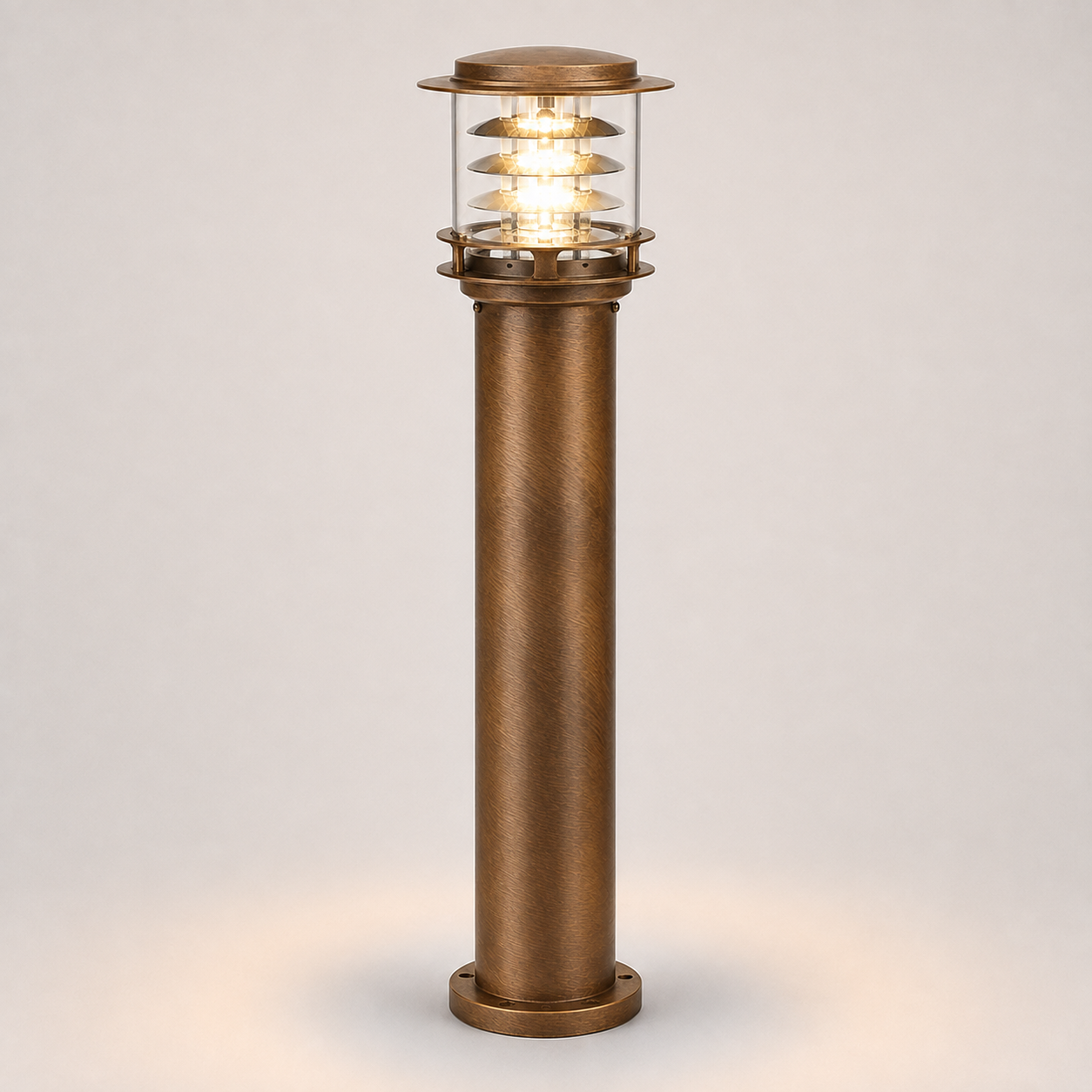 A single outdoor bollard post light with a textured bronze column and a clear glass top section showing a warm glowing light, set against a neutral light gray background.