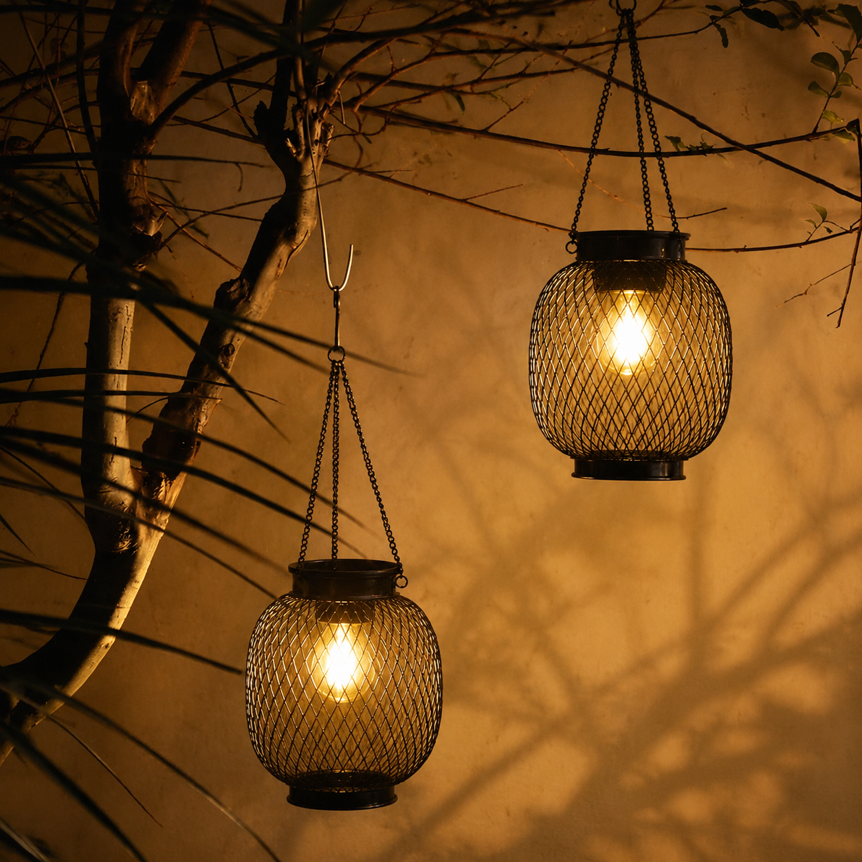 Two outdoor solar lanterns hang at different heights against a warm garden wall.