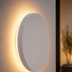 Close-up side view of a white outdoor wall light casting a warm halo on a neutral wall.