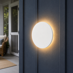 White round outdoor wall light glowing on a dark blue exterior wall beside a porch.