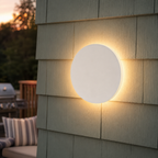 White round outdoor wall light casting a warm halo across pale gray exterior panels.