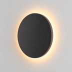 Black round outdoor wall light glowing with a warm halo against a plain light background.