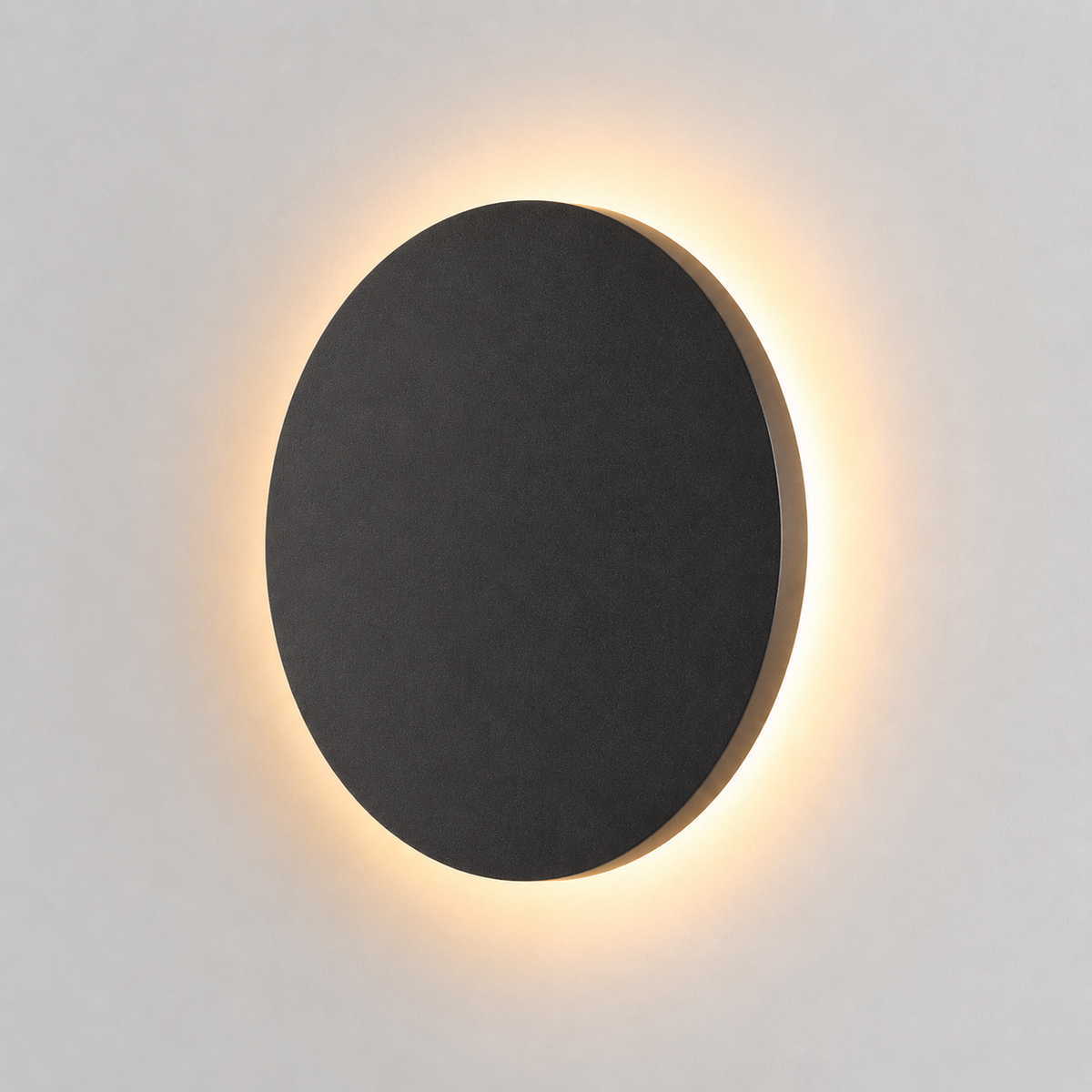 Black round outdoor wall light glowing with a warm halo against a plain light background.