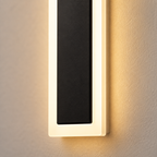 Outdoor wall sconce close-up showing a black center panel, pale frame, and warm side glow.