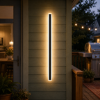 Outdoor wall sconce casting warm light on horizontal exterior siding beside a patio.