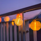Warm white paper lantern string lights hanging beneath a porch roof.