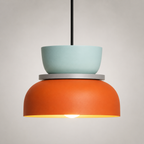 Orange and mint green color-block pendant light glowing warm white against a neutral studio background.