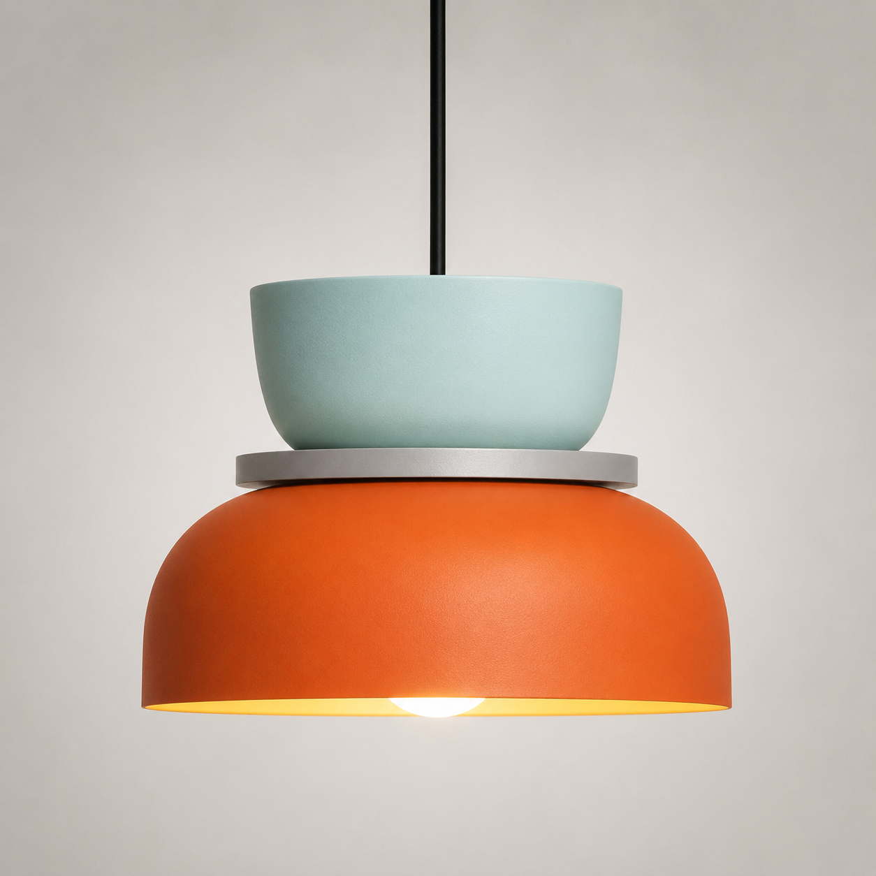 Orange and mint green color-block pendant light glowing warm white against a neutral studio background.