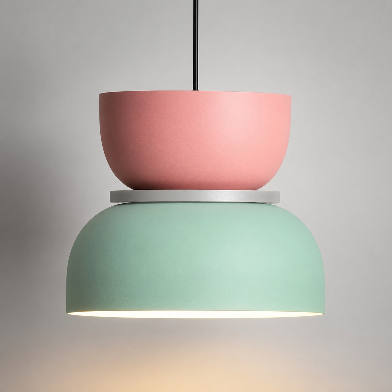 Pink and mint green color-block pendant light glowing warm white against a neutral studio background.