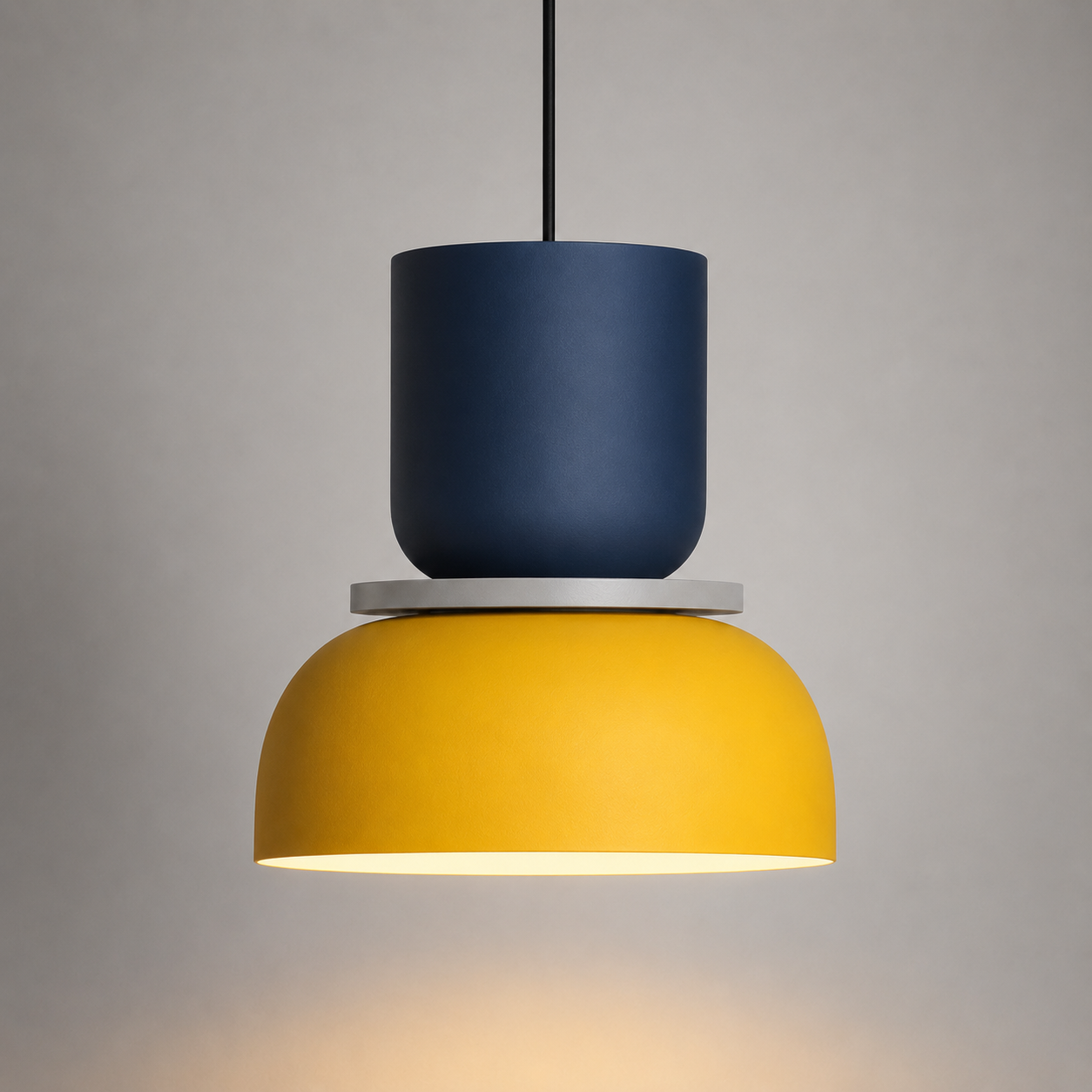 Navy and yellow color-block pendant light glowing warm white against a neutral studio background.