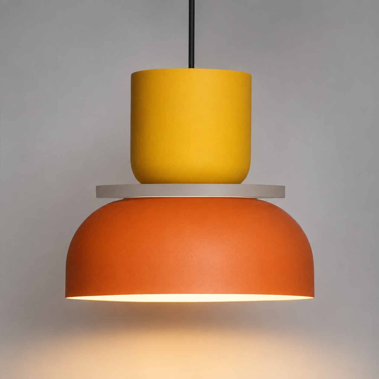 Orange and yellow color-block pendant light glowing warm white against a neutral studio background.