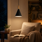 Black conical pendant light with a natural wood stem, glowing warm white above a cozy reading chair with an open book and side table.
